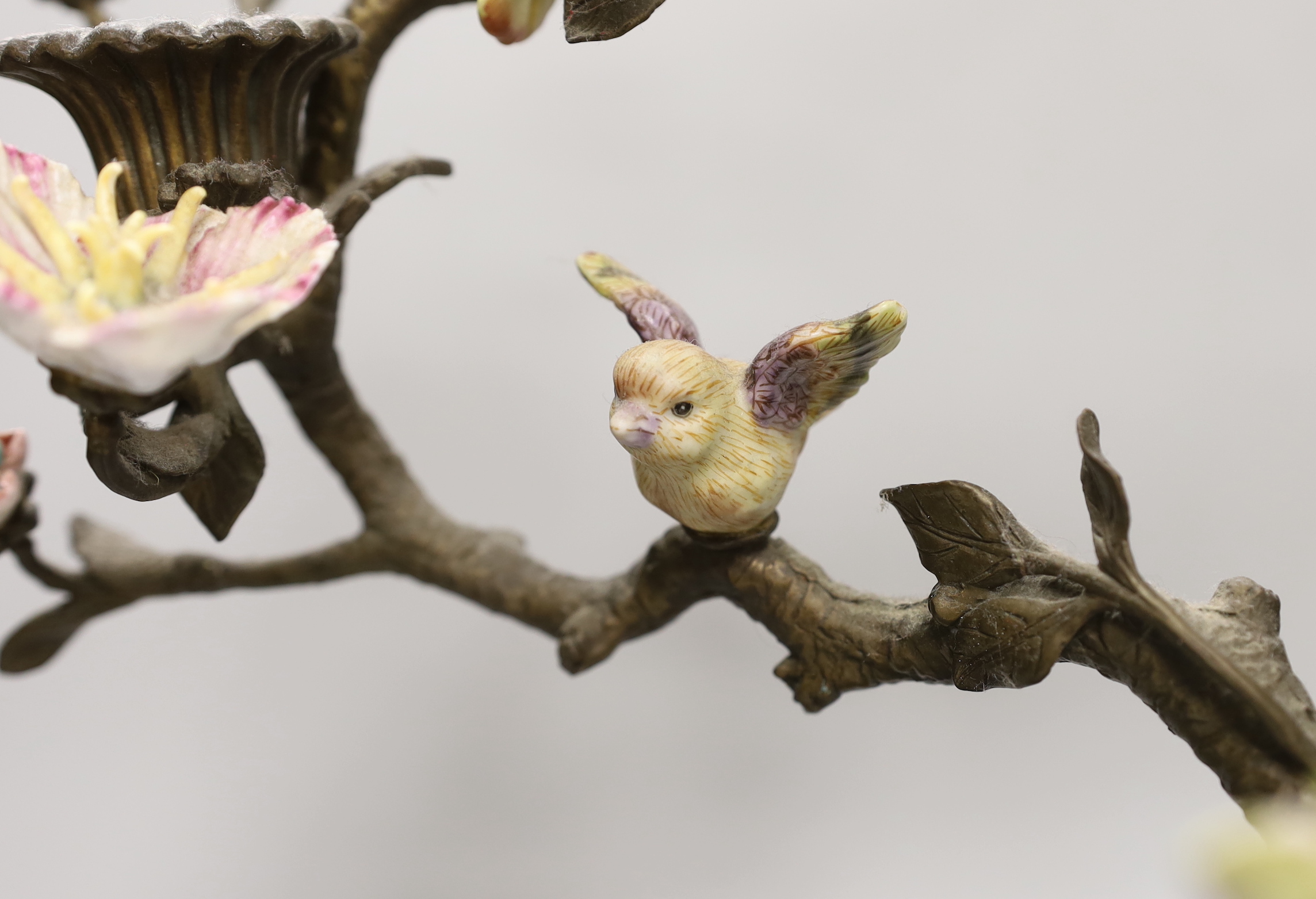 A pair of Victorian style bronzed metal and porcelain three branch candelabra, modelled as birds among branches, each 51cm high